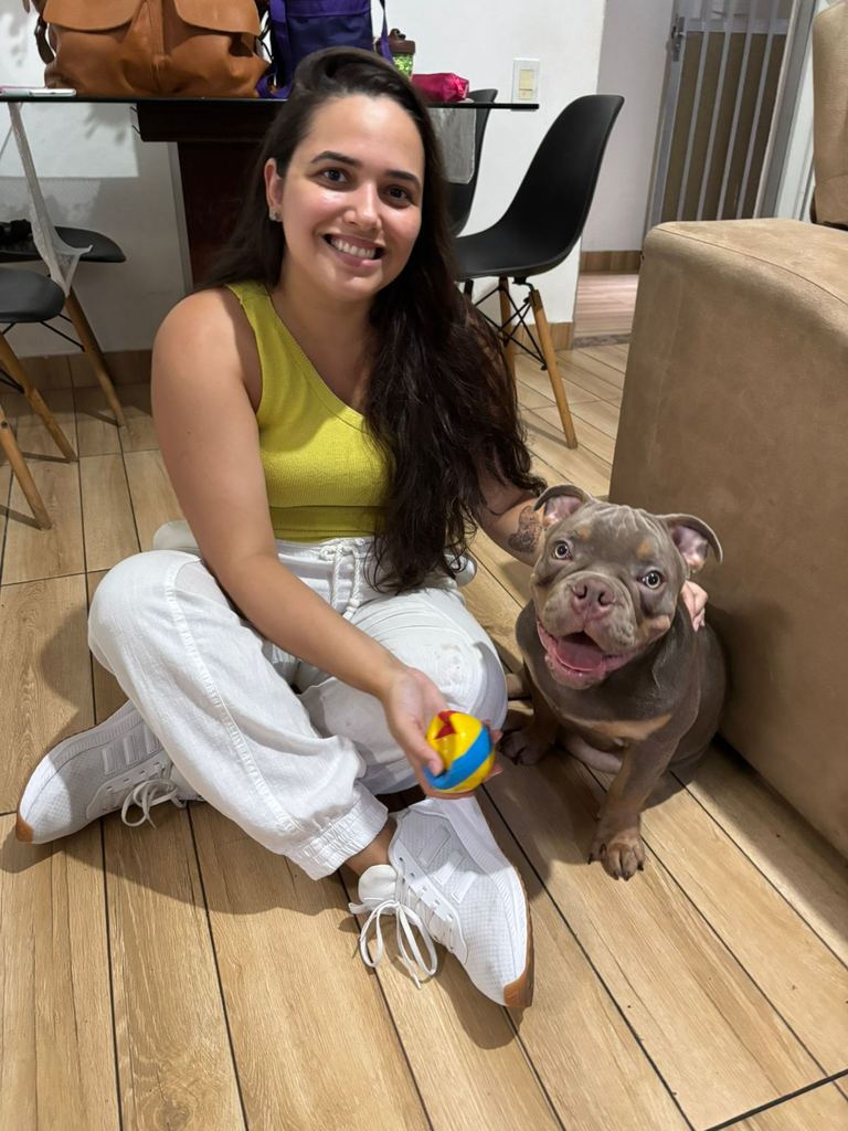 Dra. Marcella Moreira sentada no chão, sorrindo, ao lado de um cachorro durante atendimento veterinário a domicílio