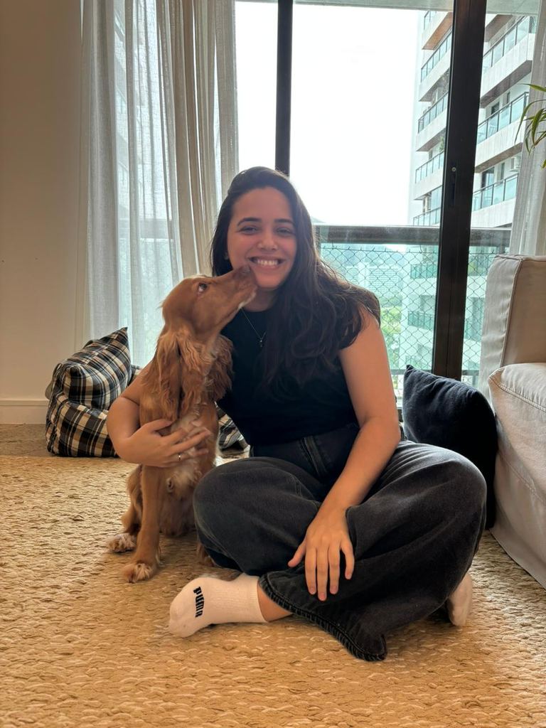 Dra. Marcella Moreira sentada no tapete com um cachorro cocker que lhe dá um beijo, em atendimento veterinário a domicílio