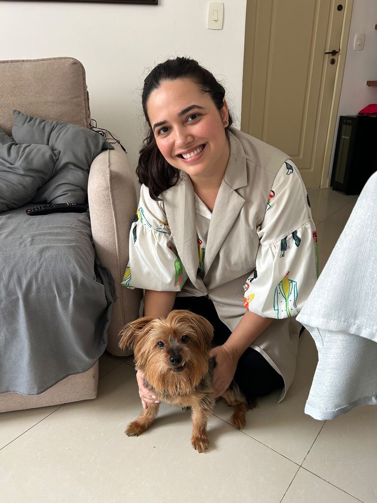 Dra. Marcella Moreira sorrindo ao lado de um cachorro yorkshire após atendimento veterinário a domicílio